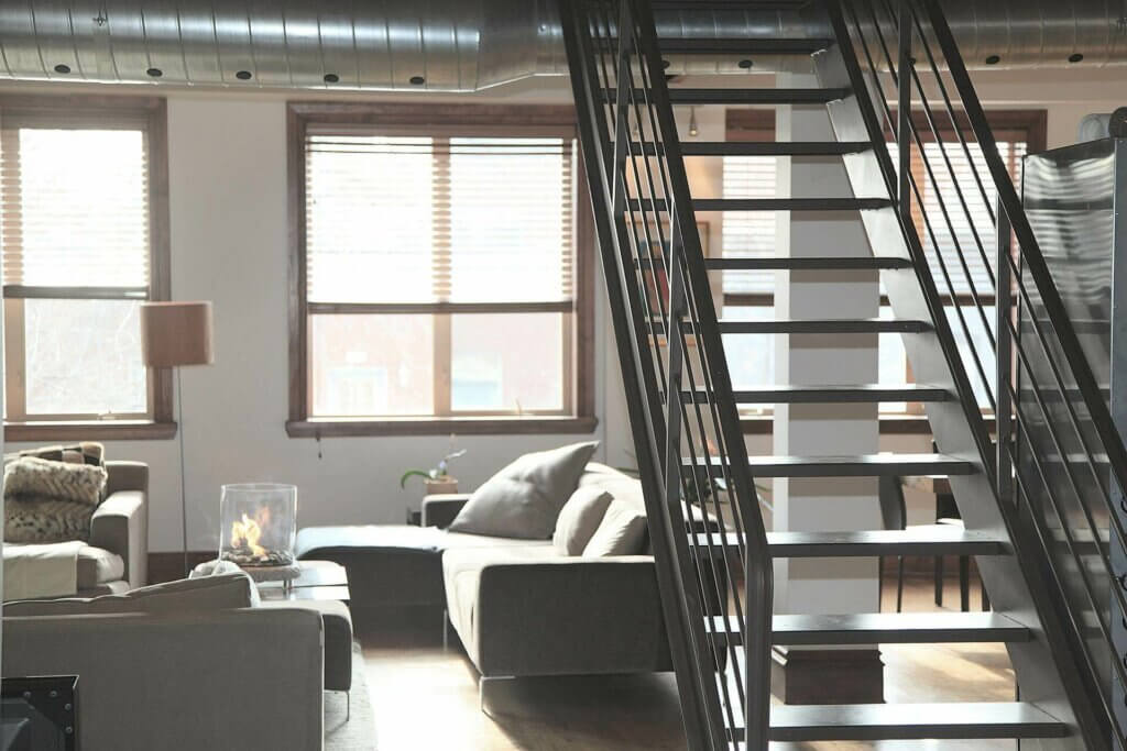 The interior of an apartment. Couches, a coffee table, and a staircase leading up to a loft are visible.