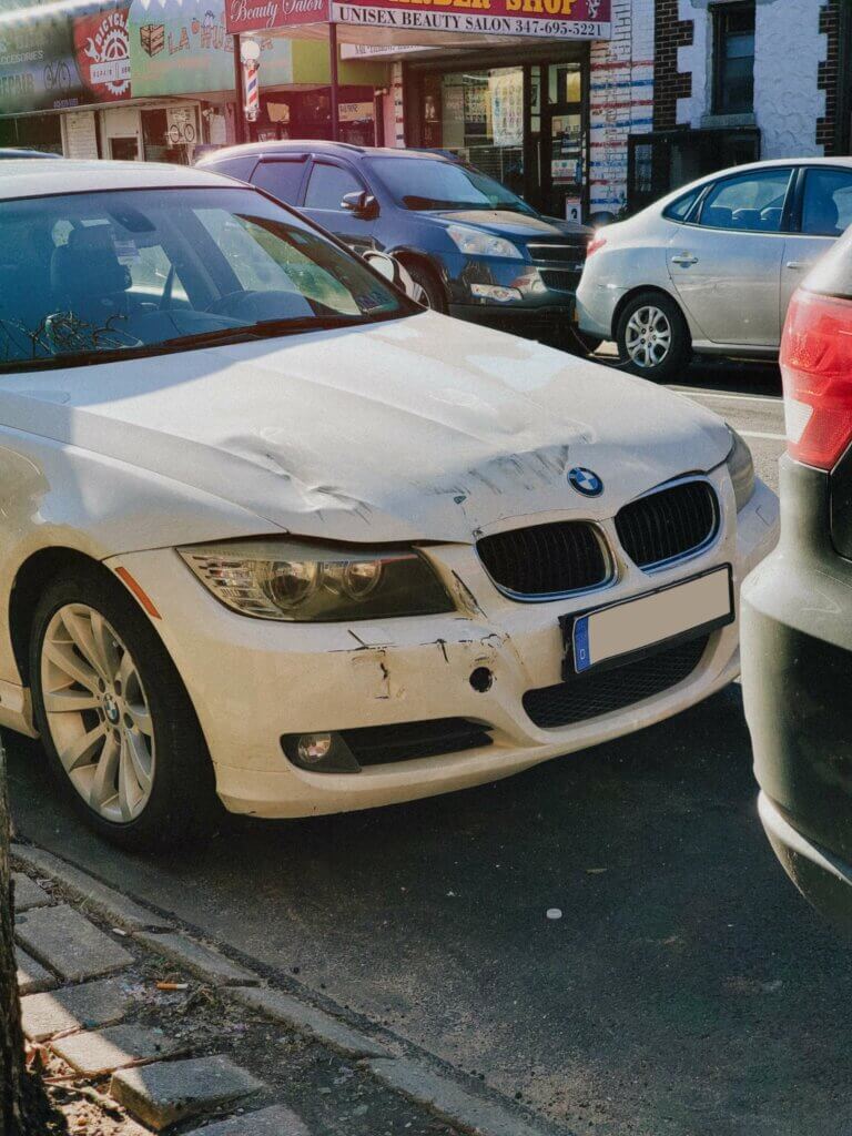 A white BMW with a dented front end. it may be totaled if there is engine damage.